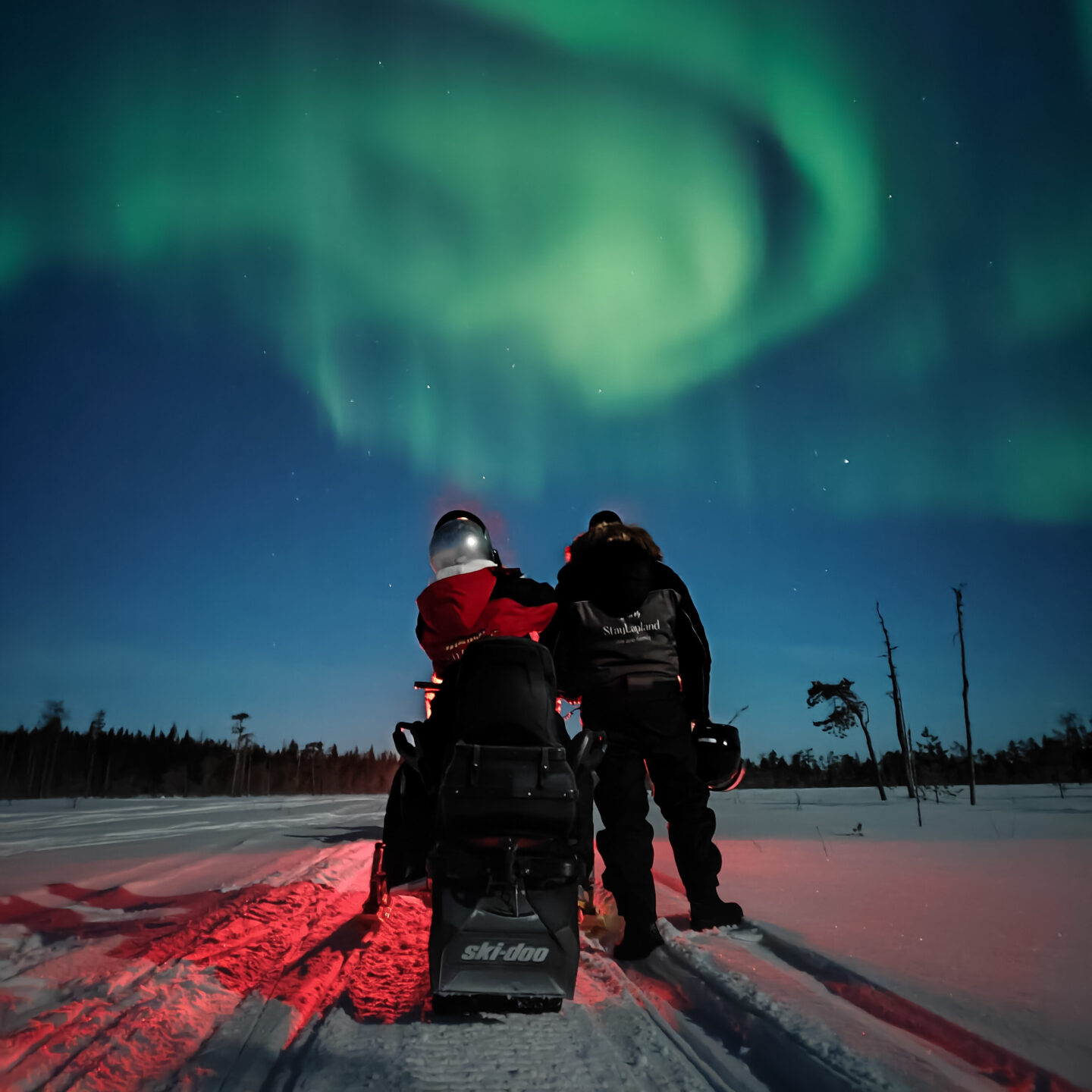 StayLapland Northern Lights with snowmobiles tour in Kuoksa Wilderness park. Activity in Rovaniemi, Lapland. People are with the snowmobile watching the aurora borealis